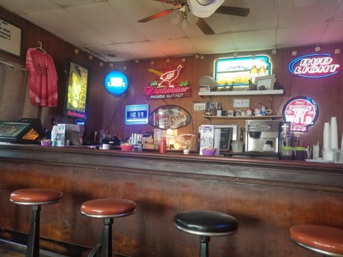 A rustic bar interior with neon signs, a wooden counter, and empty stools, creating a cozy atmosphere.