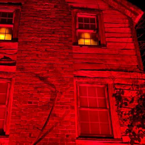 A dimly lit, old brick house with red lighting illuminating the windows, creating a spooky atmosphere.