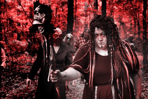 A group of eerie figures in a red-tinged forest, one holding a skull-topped staff, creating a haunting atmosphere.