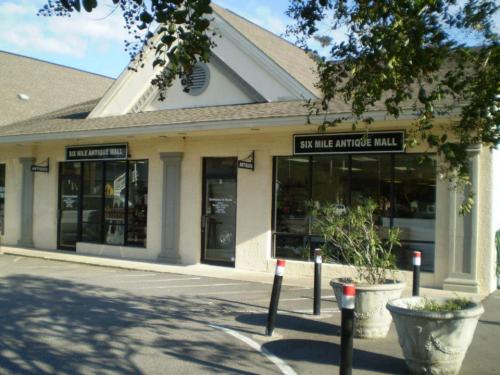 Exterior of the Six Mile Antique Mall, featuring large windows and a welcoming entrance, surrounded by greenery.