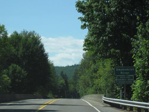 A scenic road with trees on both sides and a sign for Skokomish River Reservation ahead.