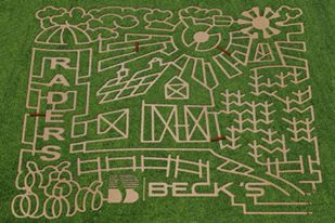 A grassy field with a maze design featuring a barn, sun, trees, and the words "RAIDERS" and "BECK'S."