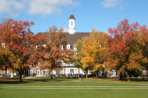 A historic building surrounded by vibrant autumn trees in shades of orange and yellow under a clear blue sky.