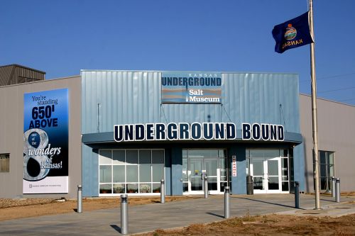 Exterior of the Kansas Underground Salt Museum, featuring a blue building and a flag, with a sign reading "UNDERGROUND BOUND."