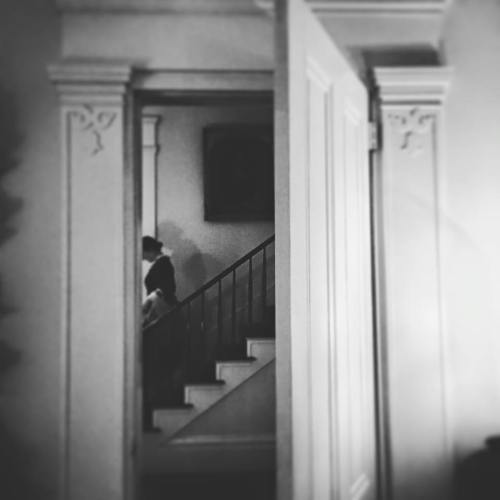 A black and white image of a person walking up a staircase, framed by an open door.