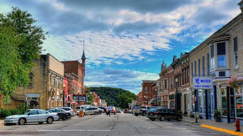 A charming small-town street lined with shops and trees under a partly cloudy sky.