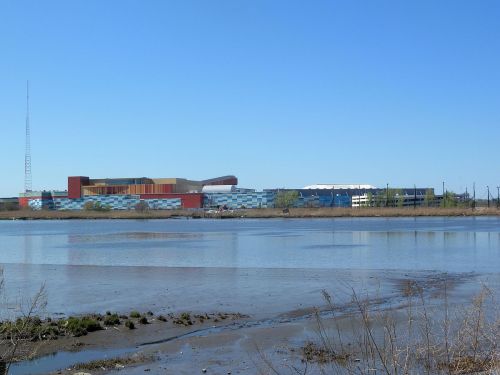 A view of a modern building complex by a calm river under a clear blue sky.
