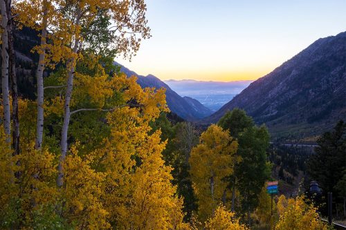 A scenic view of mountains at sunset, framed by vibrant yellow autumn trees.