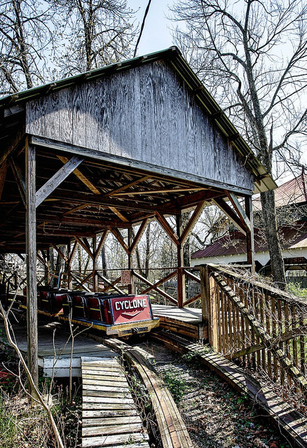 Abandoned roller coaster named "Cyclone" under a wooden shelter, surrounded by trees and overgrown pathways.