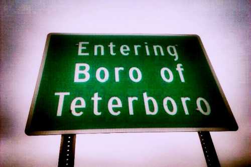 Green road sign that reads "Entering Boro of Teterboro" against a cloudy sky.