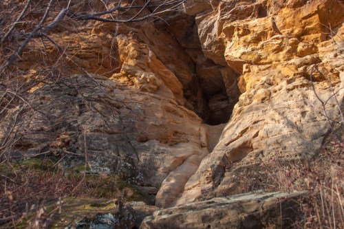 Rocky cliffside with layered sandstone formations and sparse vegetation in the foreground.