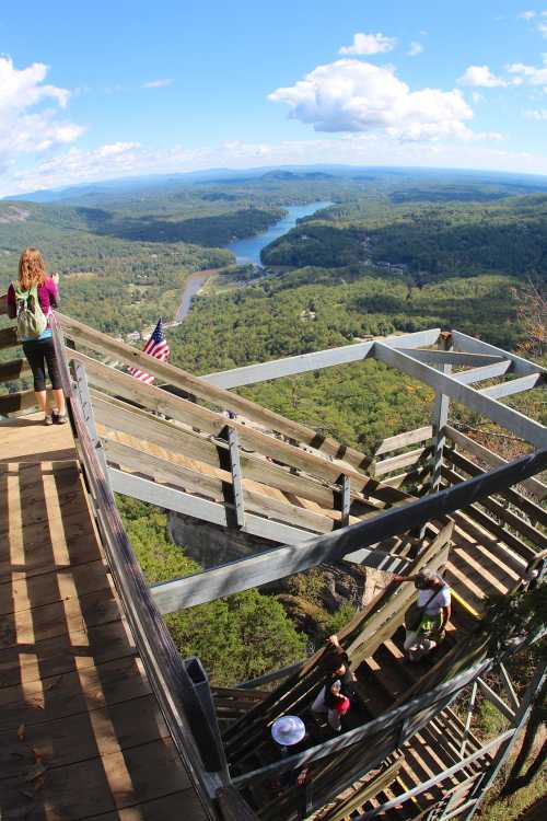 A scenic view from a wooden overlook, showing a river and lush green hills under a blue sky with clouds.