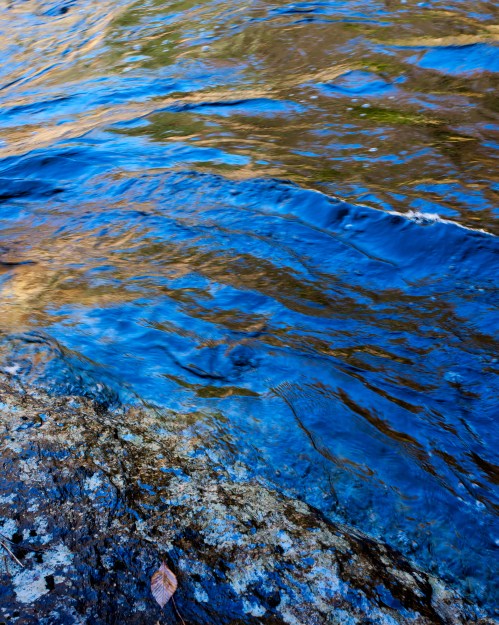 A close-up of a rocky riverbank with clear blue water gently flowing over the stones.