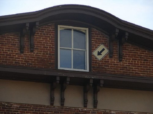 A brick building with a curved roof, featuring a window and a left-turn traffic sign above it.