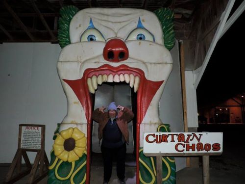 A person stands in front of a large clown entrance to a funhouse, with a sign reading "Curtain Chaos."