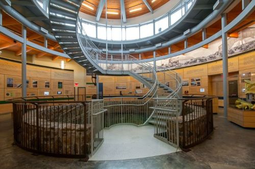 Interior view of a circular building with a spiral staircase, wooden beams, and informational displays on the walls.