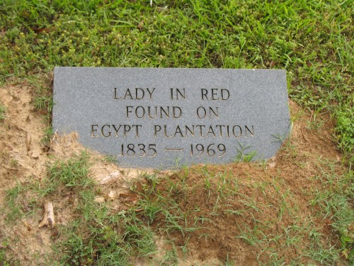 Gravestone reading "Lady in Red, Found on Egypt Plantation, 1835-1969," surrounded by grass.