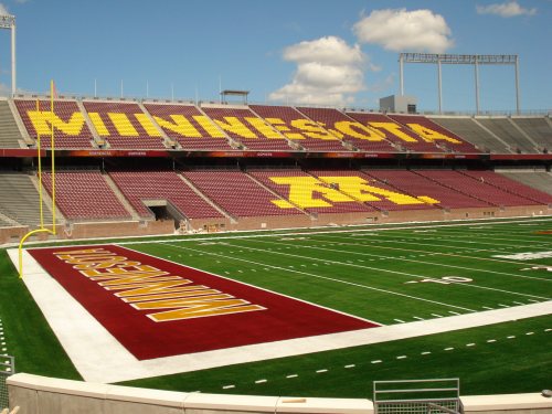 View of a football stadium with "MINNESOTA" and "GOPHERS" in large letters on the stands and a green field.