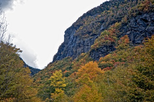 A scenic view of a mountain with colorful autumn foliage and a cloudy sky in the background.