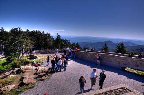 A scenic overlook with visitors enjoying the view of mountains and trees under a clear blue sky.