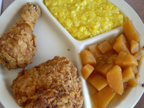 A plate with fried chicken, yellow cornmeal, and diced peaches in syrup.