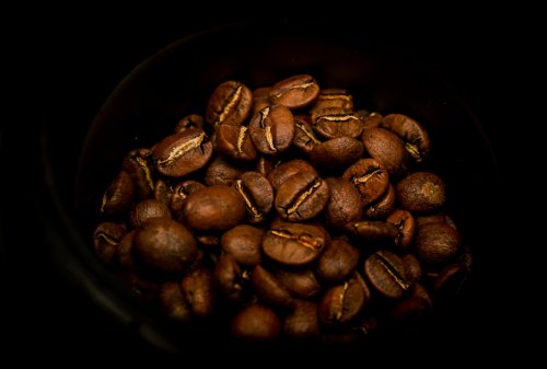 Close-up of dark roasted coffee beans in a black container, showcasing their rich texture and color.