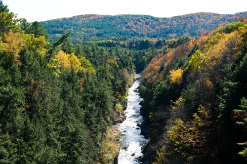 A scenic view of a river winding through a forested valley with autumn foliage on the hillsides.
