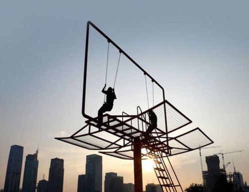 A person swings on a large structure resembling a billboard against a sunset skyline.