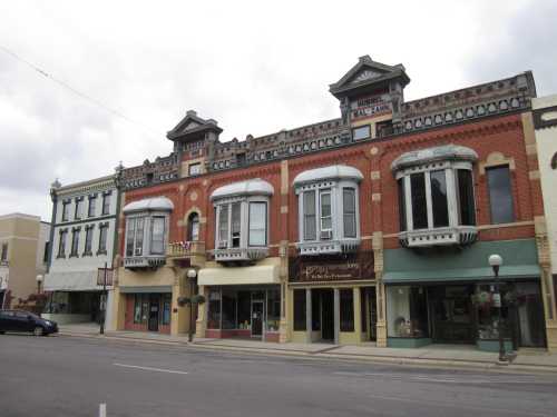 Historic brick buildings with decorative facades and large windows line a quiet street under a cloudy sky.