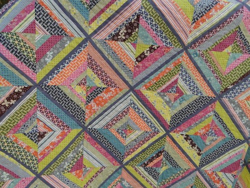 Colorful quilt featuring a geometric pattern of triangles in various fabrics and vibrant colors.