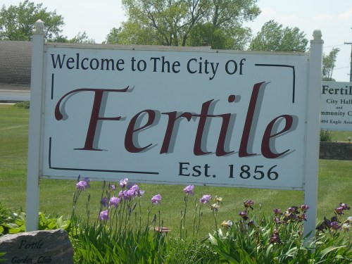 Sign welcoming visitors to the City of Fertile, established in 1856, with flowers in the foreground.