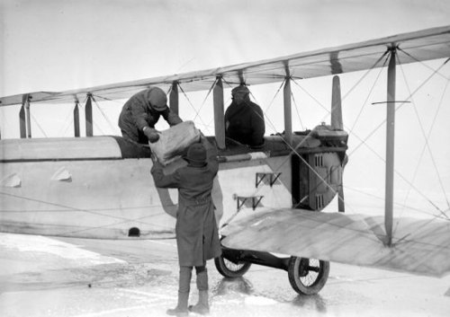 Two men in winter gear loading supplies into an early airplane on a snowy landscape.