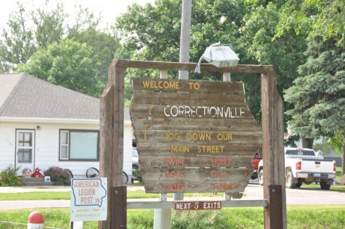Wooden sign welcoming visitors to Correctionville, listing activities like swimming, hunting, and fishing.