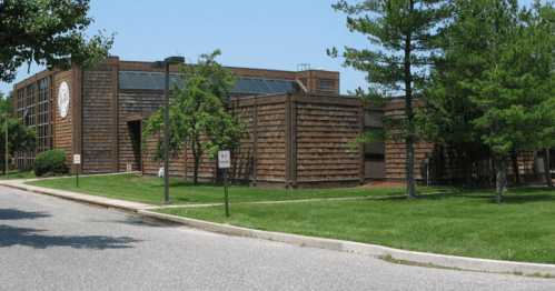 A modern building with wooden siding, surrounded by green grass and trees, on a clear sunny day.