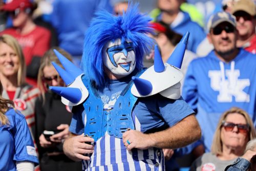A fan in blue and white face paint and spiked accessories stands out in a crowd at a sporting event.