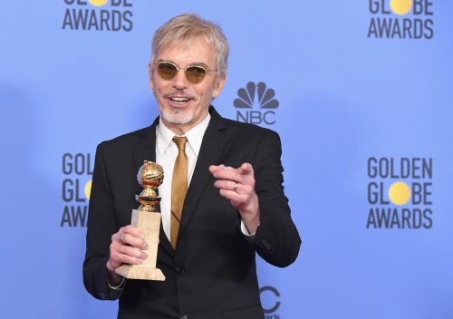 Billy Bob Thornton smiles and points while holding a Golden Globe award at the ceremony, dressed in a black suit.