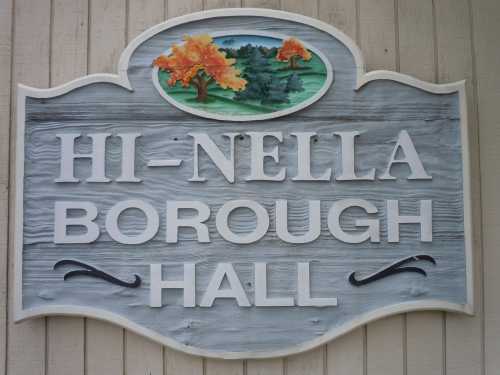 Sign for Hi-Nella Borough Hall featuring decorative trees and a scenic background.