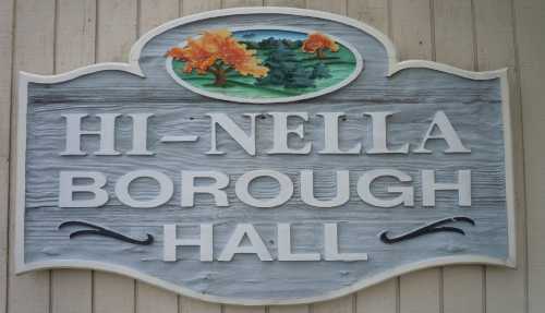 Sign for Hi-Nella Borough Hall featuring decorative trees and a scenic background.