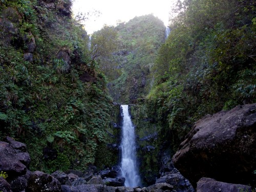 A serene waterfall cascading down rocky cliffs, surrounded by lush greenery and mist in a tranquil natural setting.