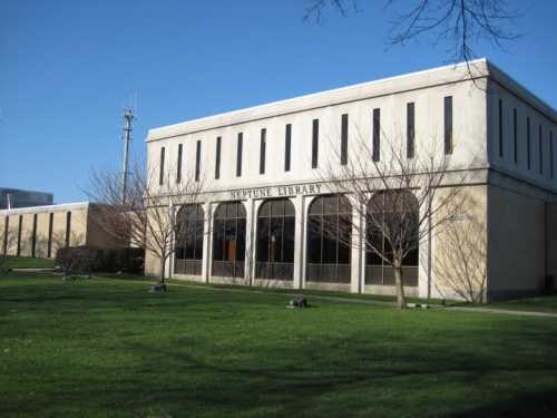 Neptune Library building with large windows, surrounded by grass and bare trees under a clear blue sky.