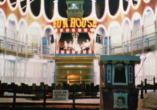 A brightly lit fun house with colorful decorations, featuring a stage and a sign that reads "Fun House."