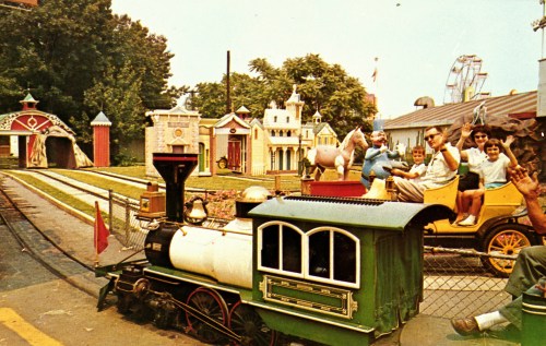 A vintage amusement park scene featuring a small train, colorful buildings, and people enjoying a ride.