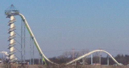 A tall water slide with a steep drop and a curved section, set against a clear blue sky.