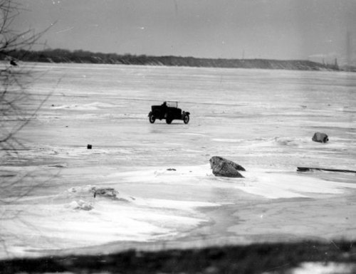A vintage car drives across a frozen landscape, surrounded by ice and large rocks.