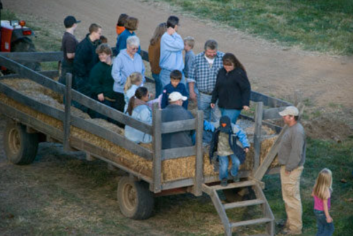 A group of people, including children, are getting off a hayride trailer in a rural setting.