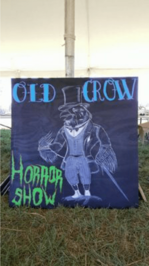 A sign for "Old Crow Horror Show" featuring a crow in a top hat and suit, set against a dark background.