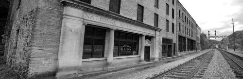 Black and white image of an old bank building beside a railway track, with a signal bridge in the background.