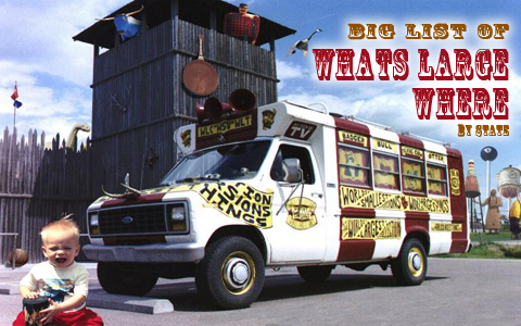 A vintage van with quirky decorations parked near a wooden structure, with a baby sitting on the ground in front.