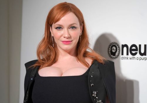A woman with red hair and a black dress poses confidently at an event, smiling at the camera.