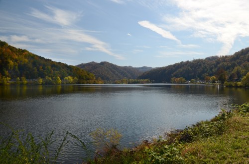 A serene lake surrounded by rolling hills and colorful autumn foliage under a clear blue sky.